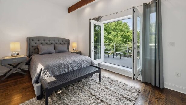 Ein Schlafzimmer mit Bett, Nachttischen, einer Bank, einem großen Fenster mit Blick ins Grüne und einer Schiebeglastür.