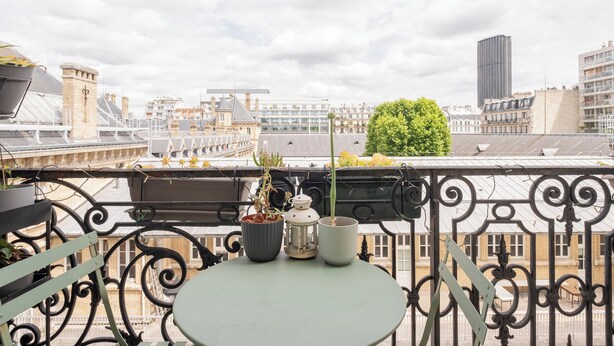 A balcony with a round table, potted plants, and a lantern.