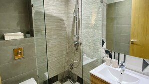 Et moderne badeværelse med en glasafskærmet bruseniche, et hvidt toilet, et træbord og et stort spejl.