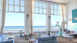 A spacious living area with large windows overlooking the sea, a dining table with chairs, and a cozy seating arrangement. - L'Émeraude Malouine (Saint-Malo)