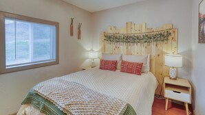 Ein Schlafzimmer mit einem Bett, zwei Nachttischen, einem Fenster und einem Holz-Kopfteil mit einer Pflanze.