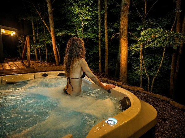 A person in a hot tub surrounded by trees at night.