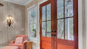 A room with a wooden paneled wall, a large wooden door with glass panels, a cushioned bench with a patterned cushion, and a small wooden stool. - Grand Pavilion 95 by Wild Dunes, Luxury Home (Isle of Palms)