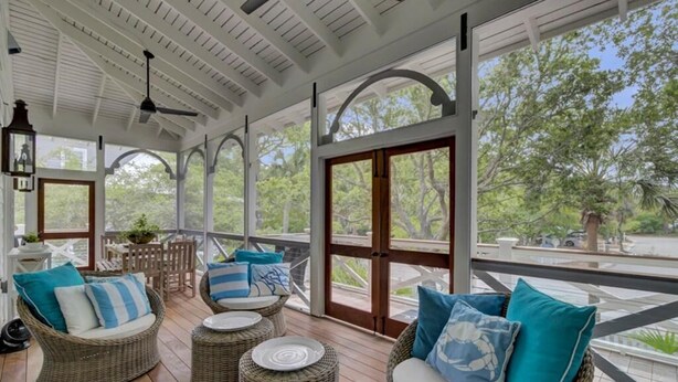 A covered outdoor area with wicker furniture, large windows, and a view of greenery. - Grand Pavilion 95 by Wild Dunes, Luxury Home (Isle of Palms)