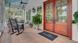 A covered porch with a rocking chair, a dining table, and a large potted plant. - Grand Pavilion 95 by Wild Dunes, Luxury Home (Isle of Palms)