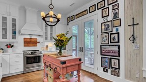 A kitchen with white cabinets, a pink wooden table, and a chandelier. - Grand Pavilion 95 by Wild Dunes, Luxury Home (Isle of Palms)