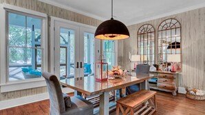 A spacious kitchen with a large wooden table, a hanging pendant light, and a view of the outdoors through large windows. - Grand Pavilion 95 by Wild Dunes, Luxury Home (Isle of Palms)