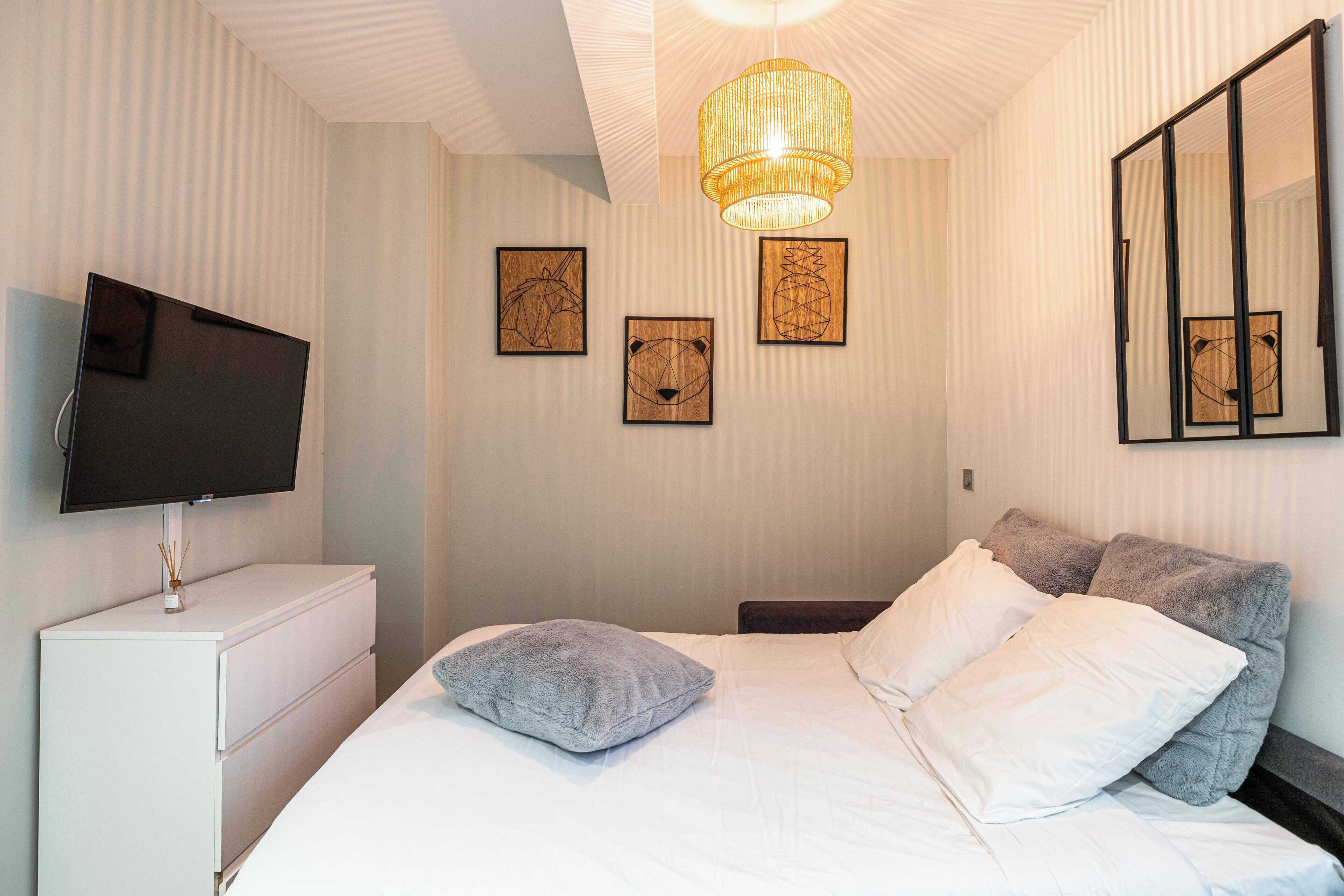 Une chambre bien rangée, avec un lit, des oreillers, un téléviseur et des œuvres d’art accrochées au mur.