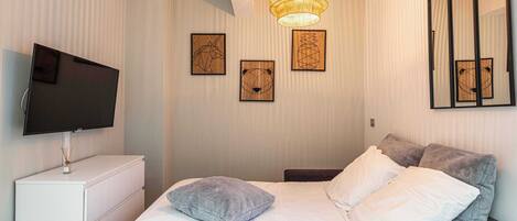 Une chambre bien rangée, avec un lit, des oreillers, un téléviseur et des œuvres d’art accrochées au mur.