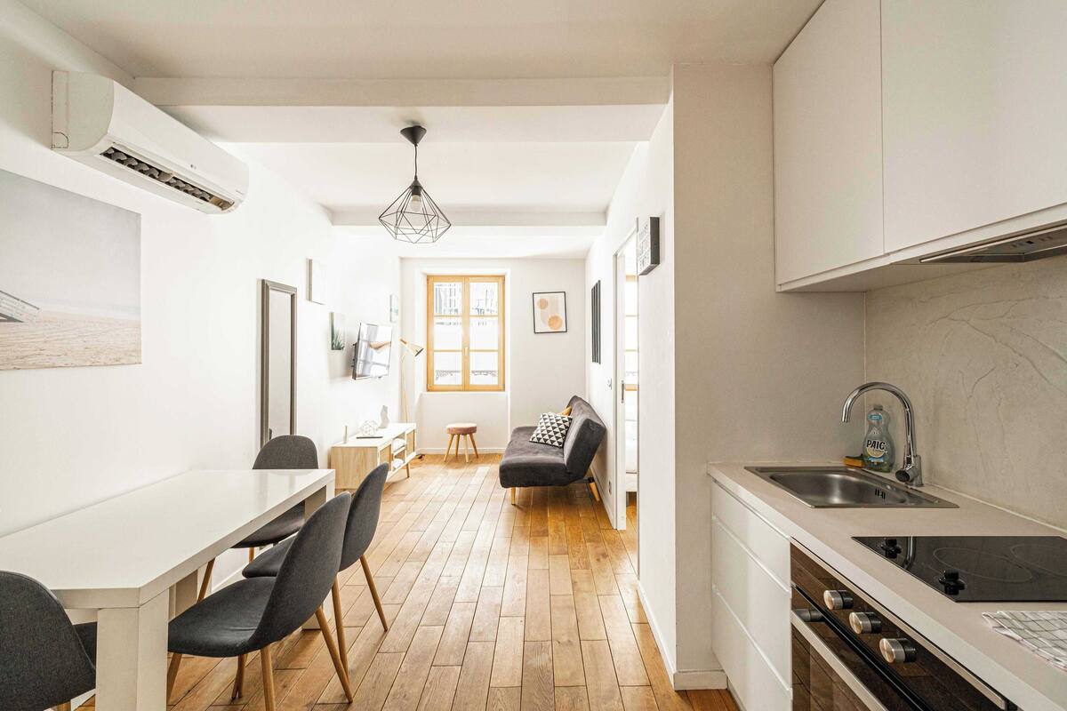 A modern kitchen with a dining area, wooden flooring, and a view to the living room.