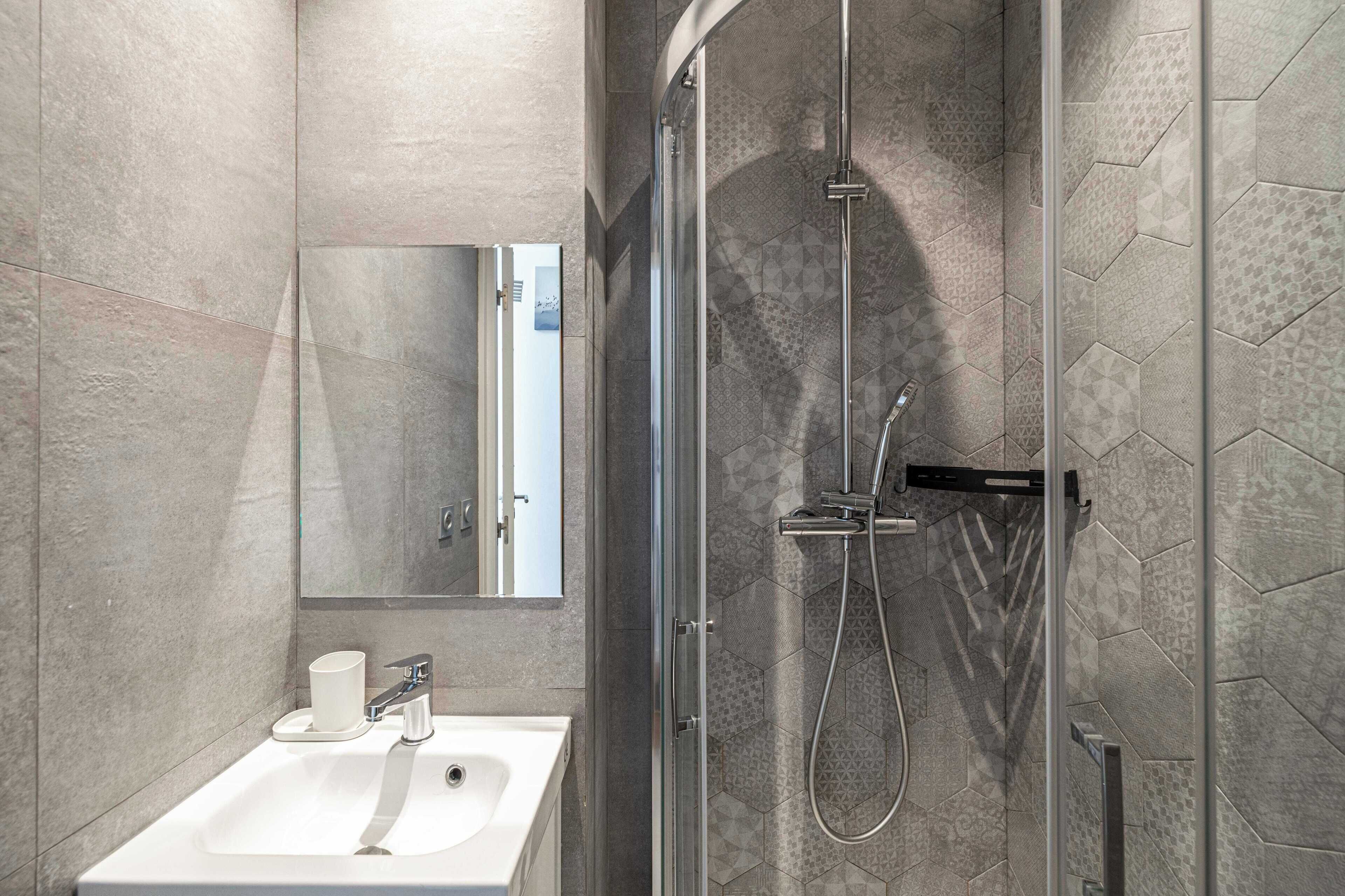 A modern bathroom with a glass-enclosed shower, a white sink, and a large mirror.