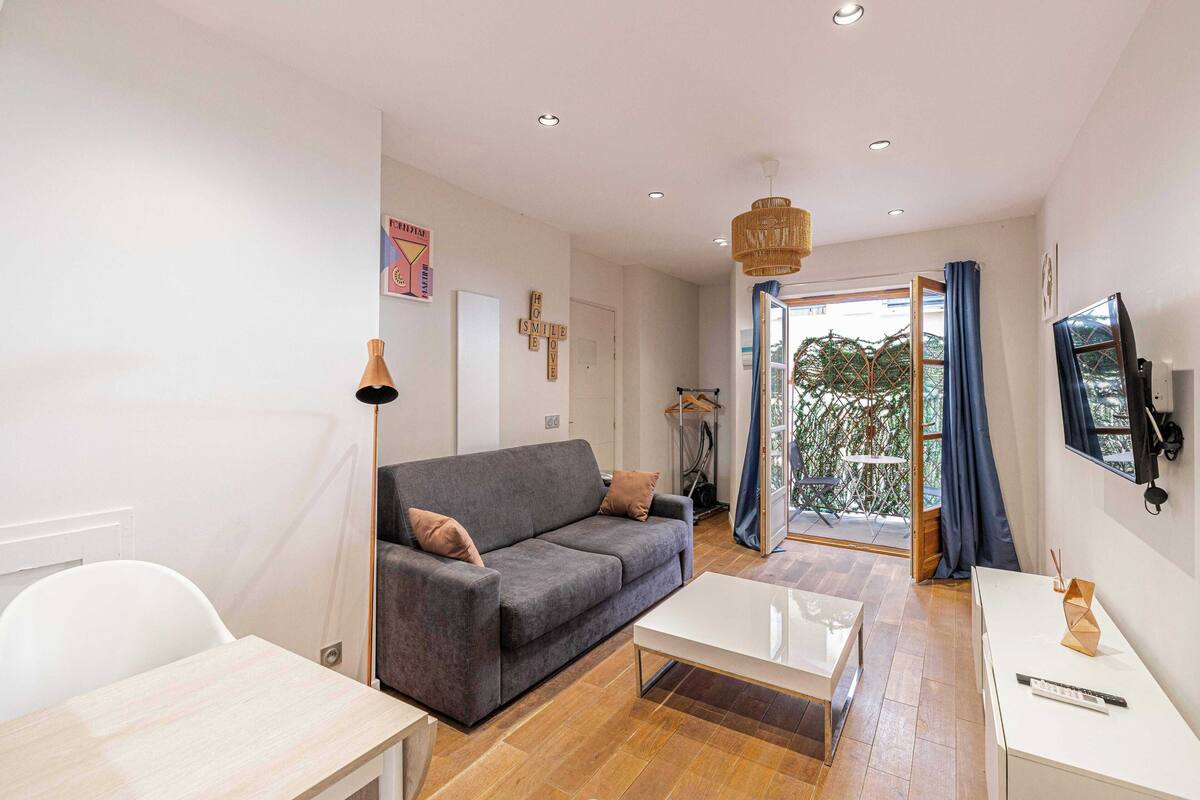 A modern living room with a grey sofa, white coffee table, and a TV on the wall.