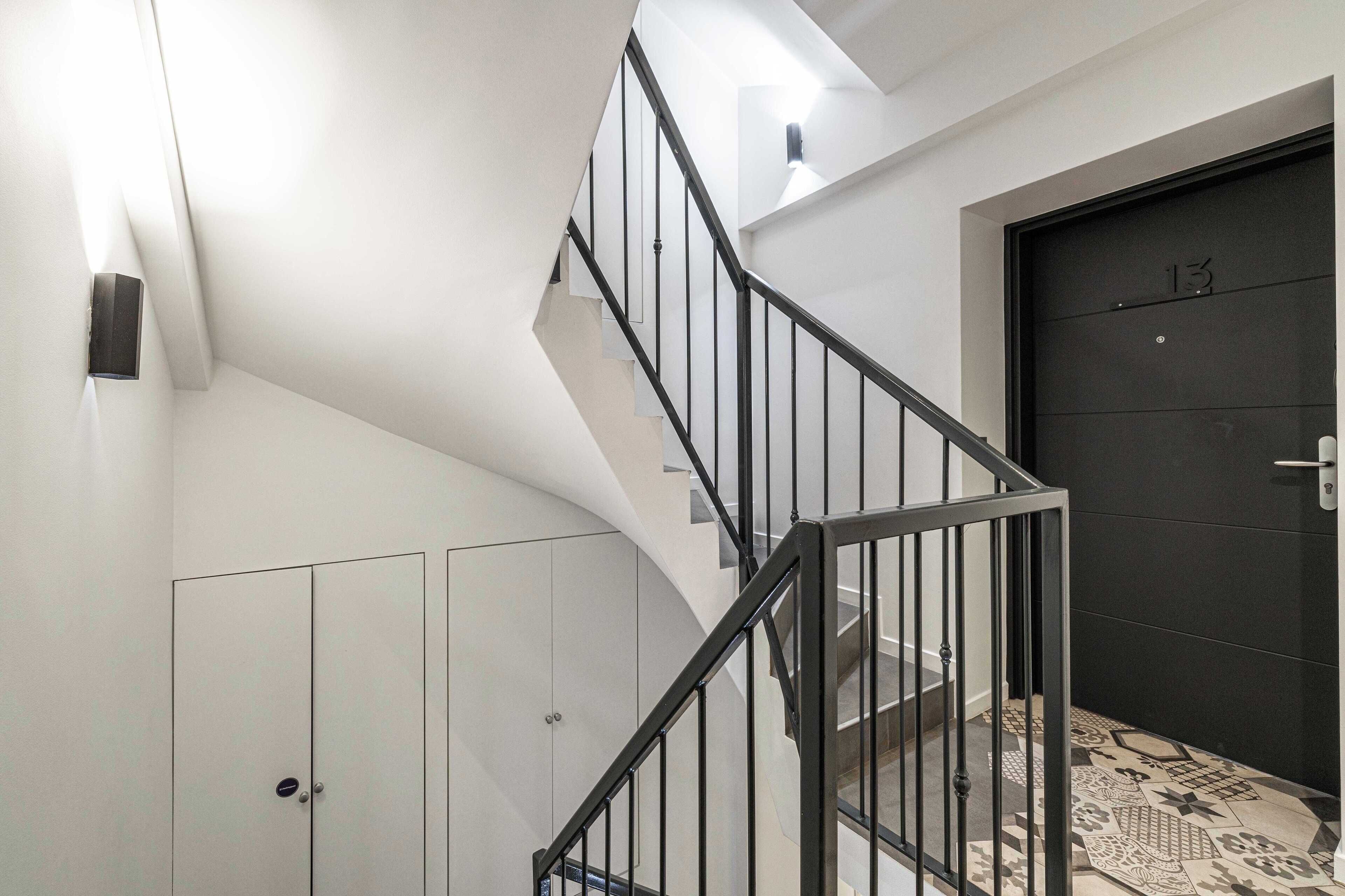 A modern staircase with black railings, a dark door with the number 13, and a patterned floor.