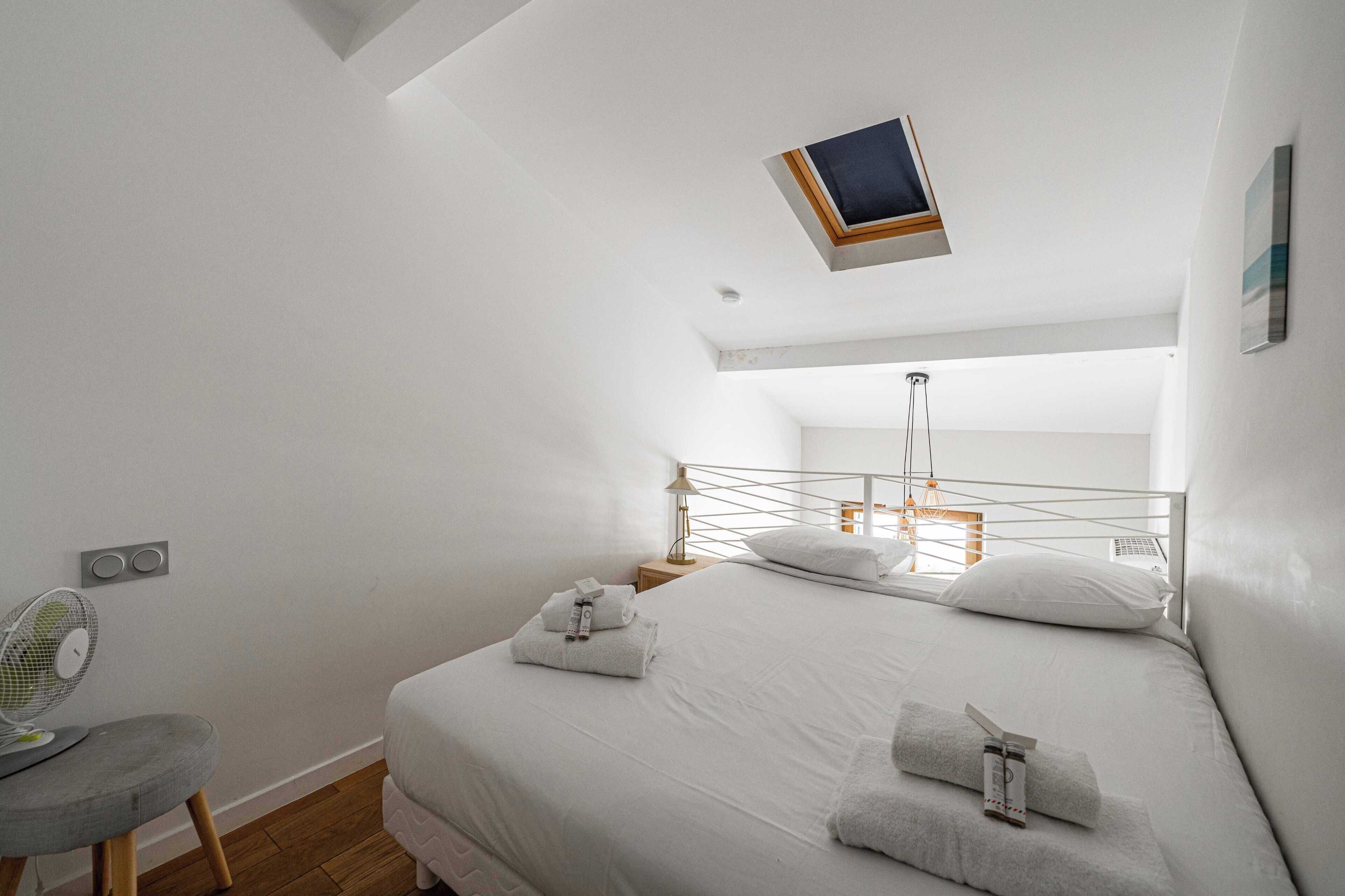 A bedroom with a bed, a chair, a fan, and a small table.
