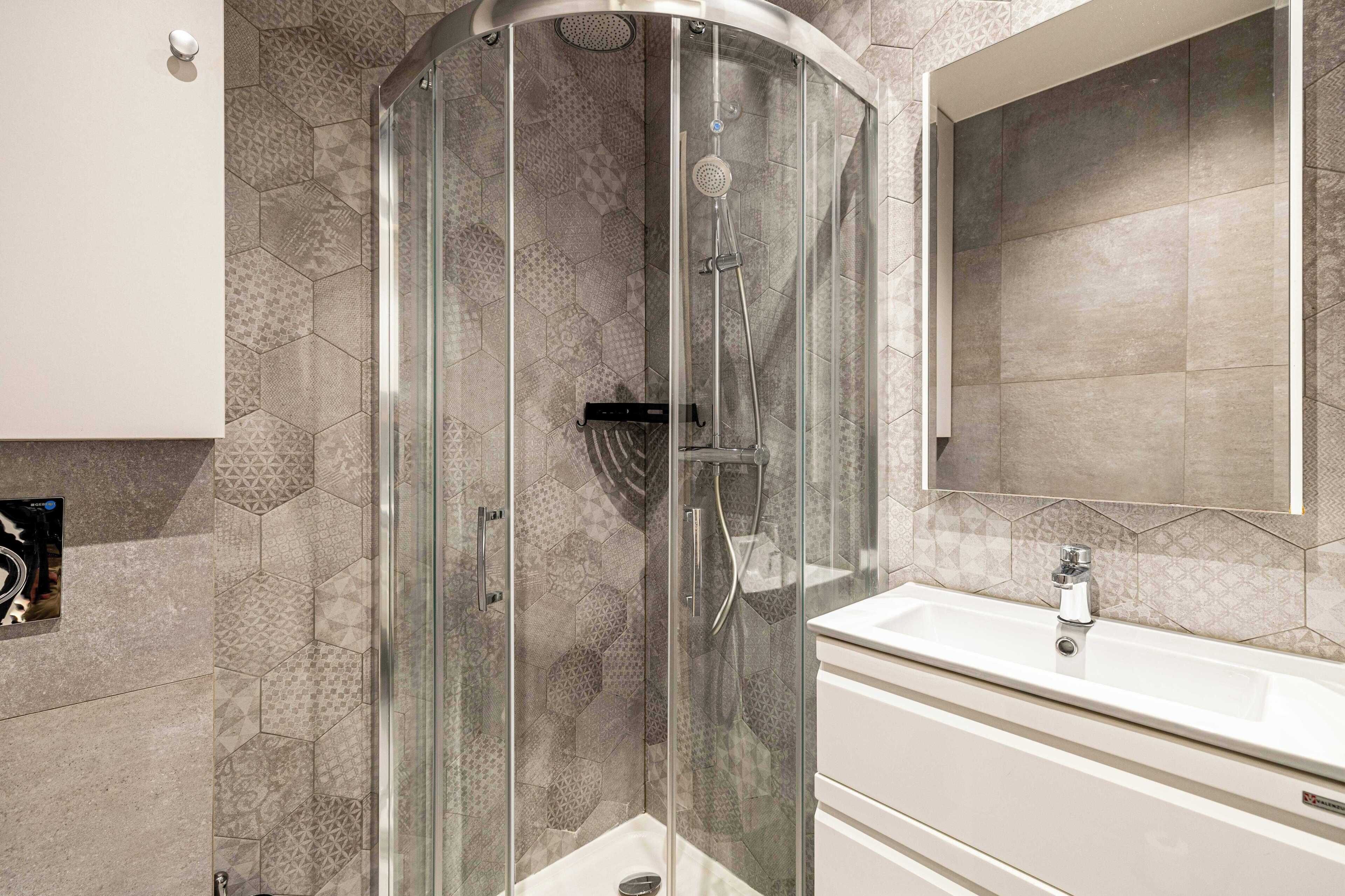 A modern bathroom with a glass-enclosed shower, a white sink, and a large mirror.