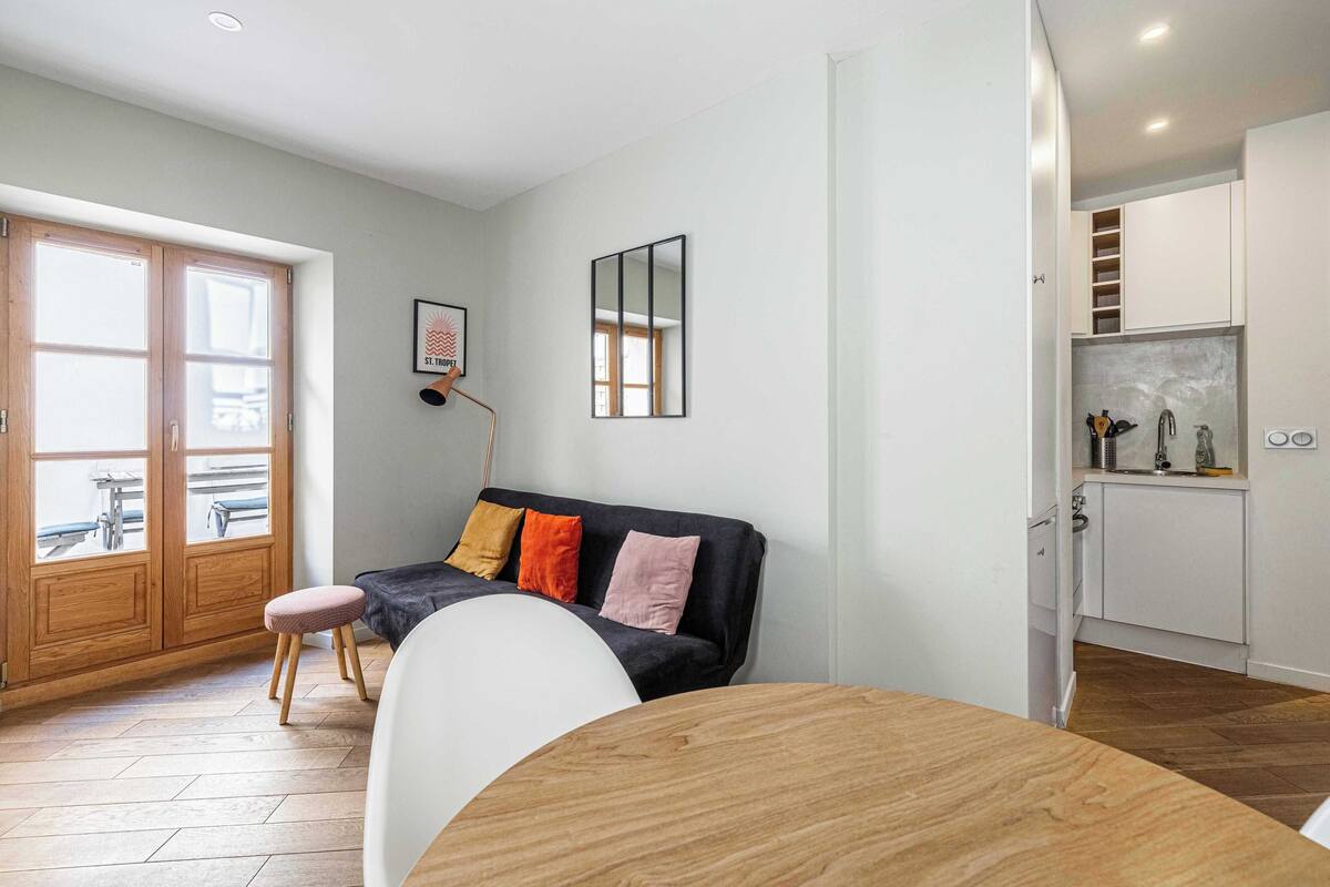 A modern living room with a sofa, a dining table, and a kitchen area.