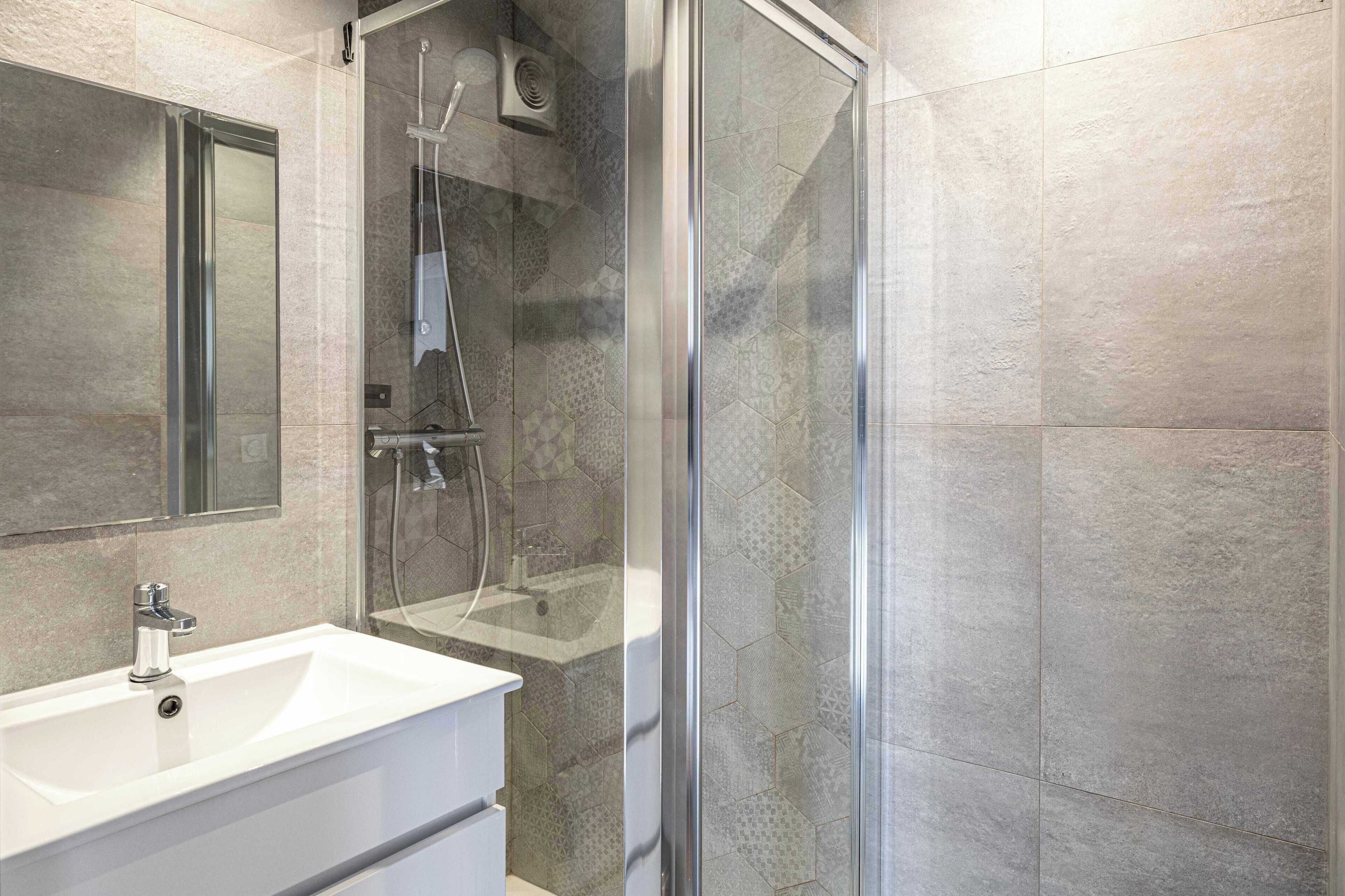 Une salle de bain moderne avec une douche à l’italienne en verre, un lavabo blanc et un grand miroir.
