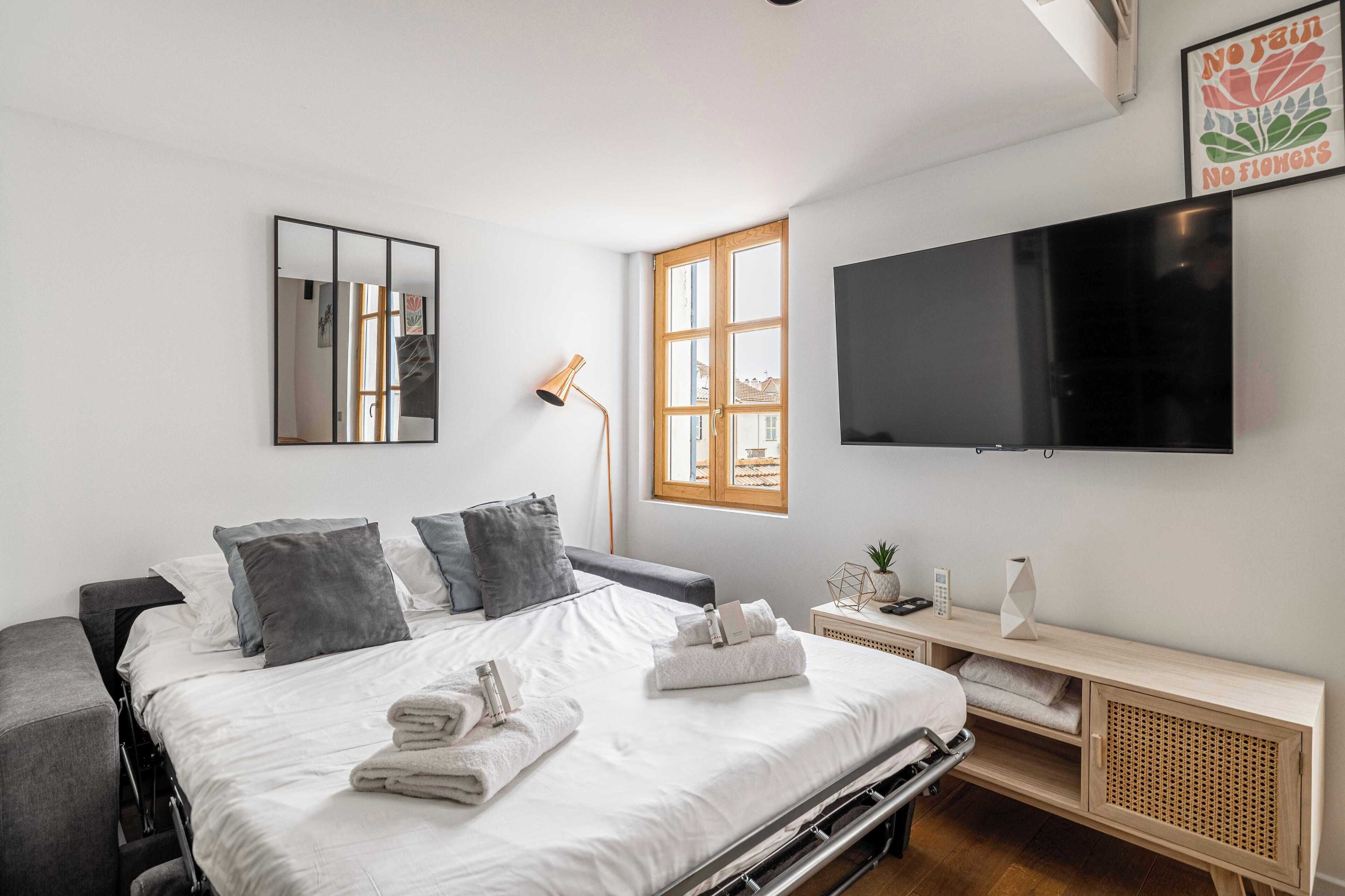 Ein modernes Schlafzimmer mit Bett, Nachttisch, Fernseher und einem Fenster.