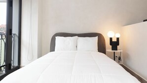 Ein ordentlich bezogenes Bett mit weißer Bettwäsche, einem grauen Kopfteil und einem Nachttisch mit zwei kugelförmigen Lampen.