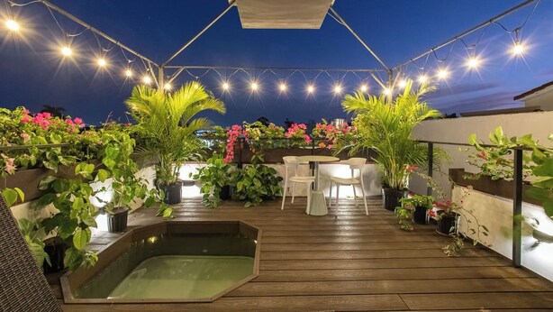 Ein Terrassenbereich im Freien mit Holzboden, Blumentöpfen, einem kleinen Pool und Lichterketten.