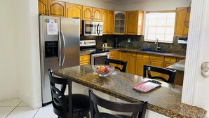 A modern kitchen with granite countertops, stainless steel appliances, wooden cabinets, and a breakfast bar with two chairs.