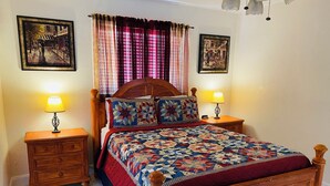 A bedroom with a wooden bed, two bedside tables with lamps, a quilt, and two framed pictures on the walls.