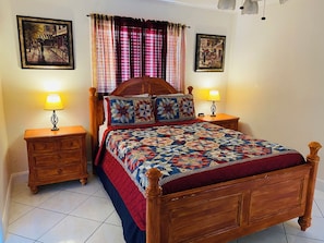 A bedroom with a wooden bed, two bedside tables with lamps, a quilt, and two framed pictures on the walls.