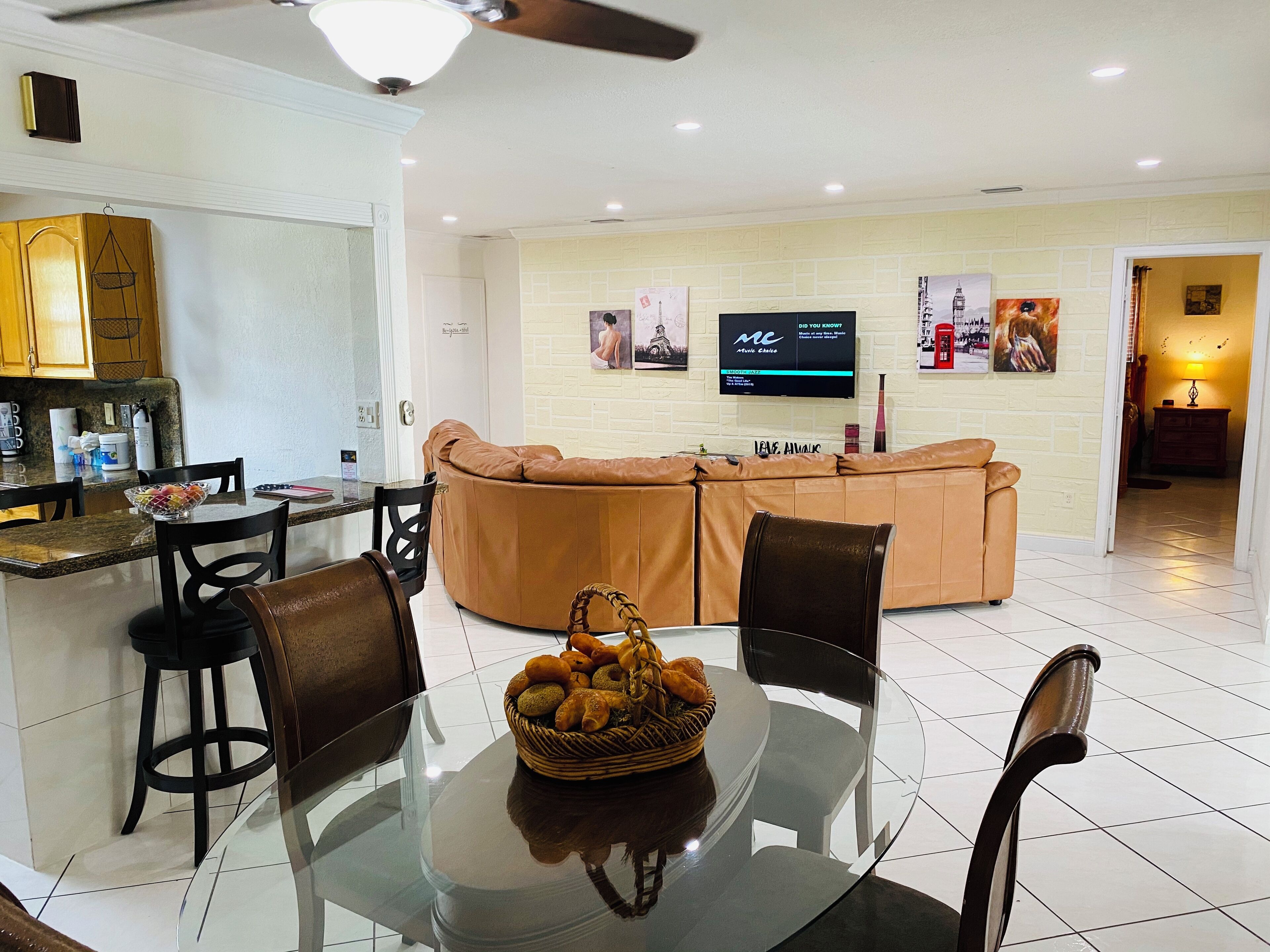 A modern living room with a glass dining table, leather sofa, and a TV mounted on the wall.