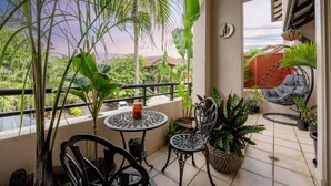A balcony with a table, chairs, potted plants, and a hanging chair.