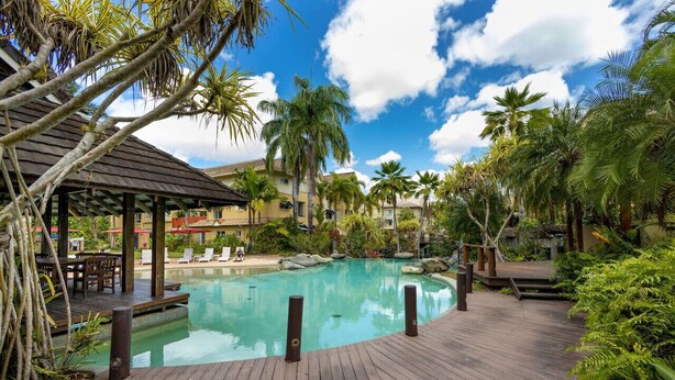 A pool area with a wooden deck, palm trees, and a covered seating area.