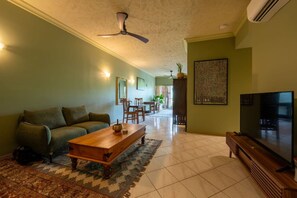 A living room with a sofa, coffee table, TV, and ceiling fan. - Stylish One-Bedroom Resort Apartment with Pools & Gardens | Lily Lakes (Cairns North)