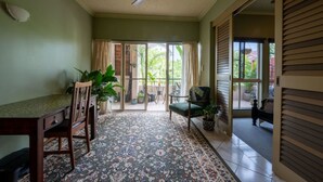 A room with a ceiling fan, a dining table with chairs, a patterned rug, and a view through a glass door to an outdoor area with plants.