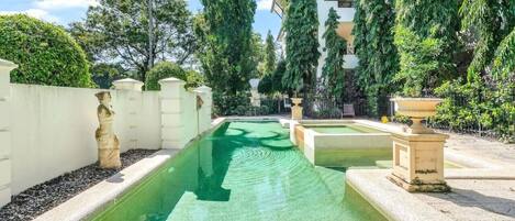 Piscina con fuente, rodeada de follaje y un edificio.