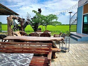 An outdoor seating area with rustic wooden furniture, a patterned tablecloth, and a view of a green field. - Chai Na Resort (Bangkok)