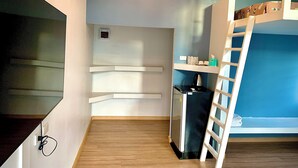 Une petite chambre comprenant un lit superposé, un coin cuisine et un téléviseur.