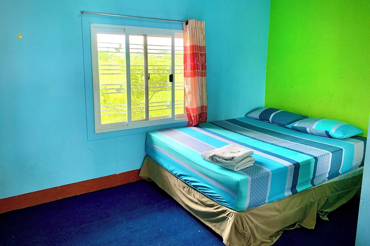 Ein Schlafzimmer mit Bett, Fenster und Blick auf Grünfläche.