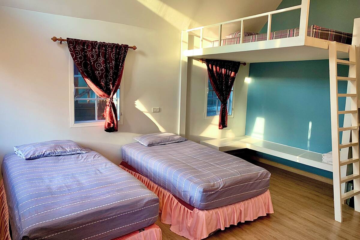 Ein Schlafsaalzimmer mit zwei Einzelbetten, einem Etagenbett und einem Fenster mit Vorhängen.