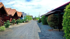 Une rue de village bordée de maisons traditionnelles en bois, un chemin de gravier et une végétation luxuriante.