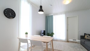 Een moderne woonkamer met een eethoek, met een houten tafel, witte stoelen, een zwarte klok en een grijze bank.