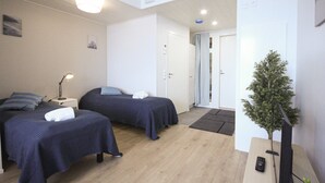 Een hotelkamer met twee bedden, een klein bureau, een lamp, een televisie en een potplant.