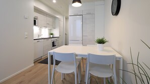 Een moderne keuken met witte kastjes, een eettafel met vier stoelen, een hanglamp en een klok aan de muur.