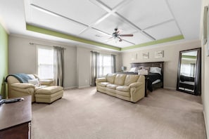 Une chambre à coucher avec un lit, un ventilateur de plafond et une grande fenêtre avec des rideaux.