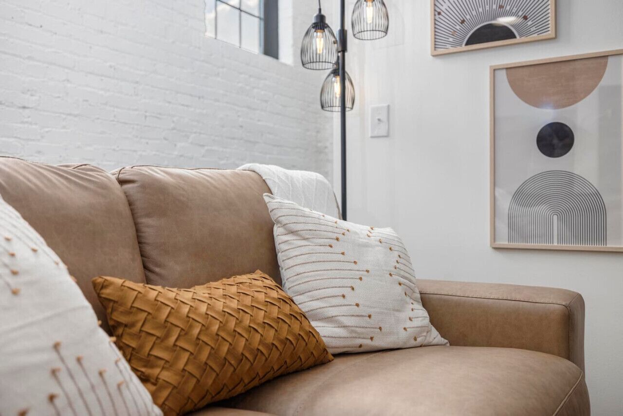 Una sala de estar moderna con un sofá color beige, un cojín tejido y un cojín blanco con un estampado discreto.