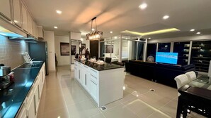 Una cocina moderna con una isla central, una zona de comedor con sofá oscuro y una sala de estar con televisor.