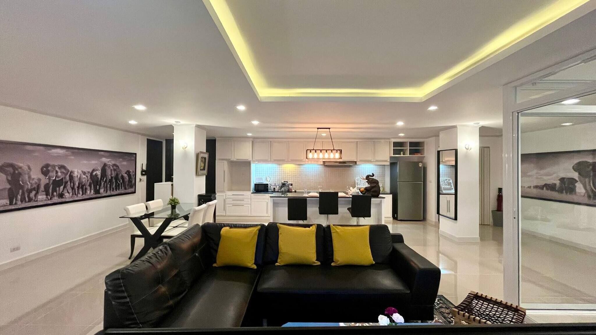 A modern living room with a black sofa, yellow cushions, and a glass coffee table.