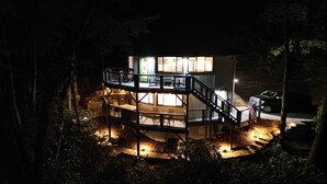 Una cabaña de madera de varios niveles con balcón, rodeada de árboles e iluminada por una luz cálida.