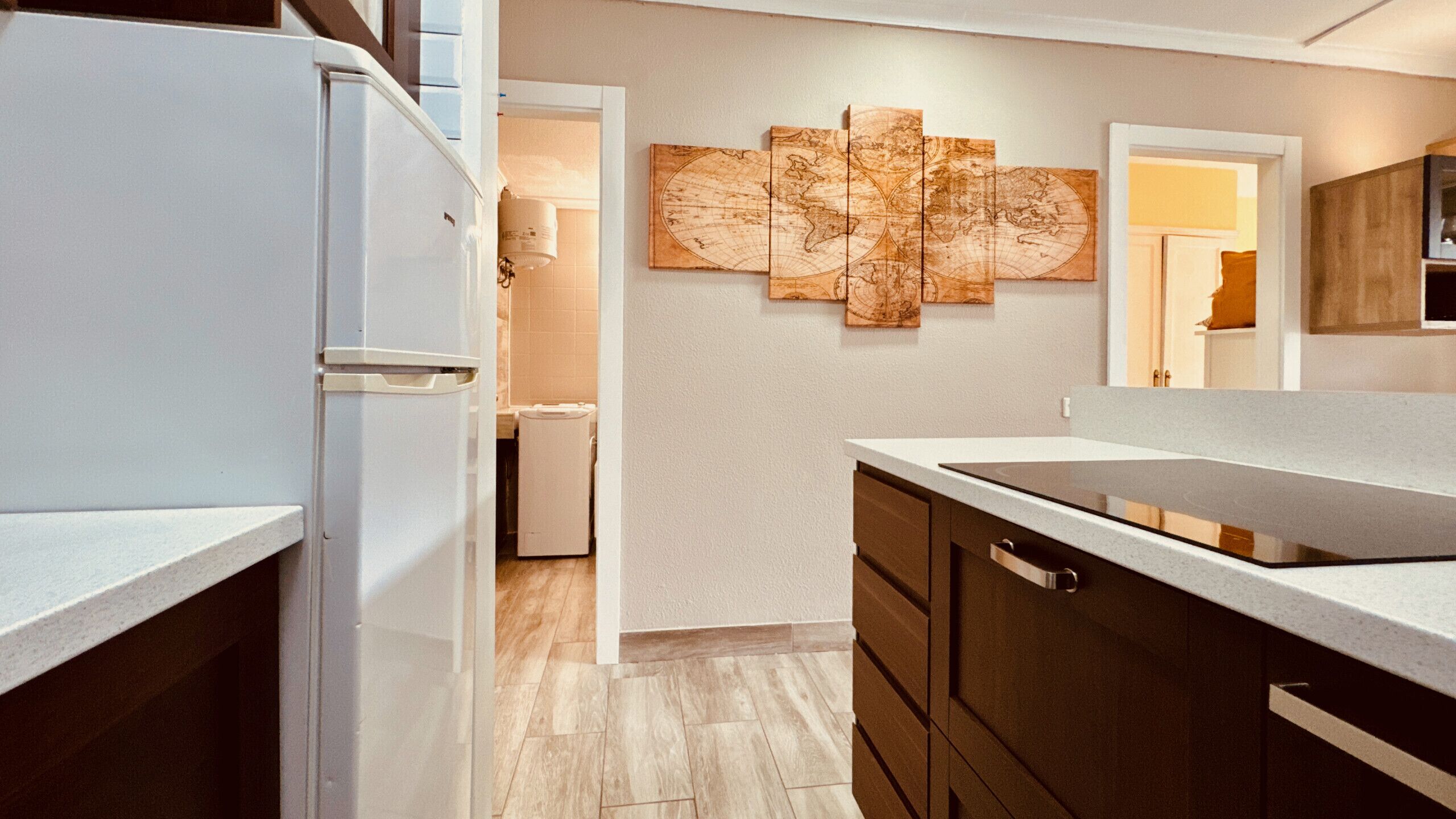 A modern kitchen with a white refrigerator, wooden cabinets, a large island, and a wall-mounted map artwork.
