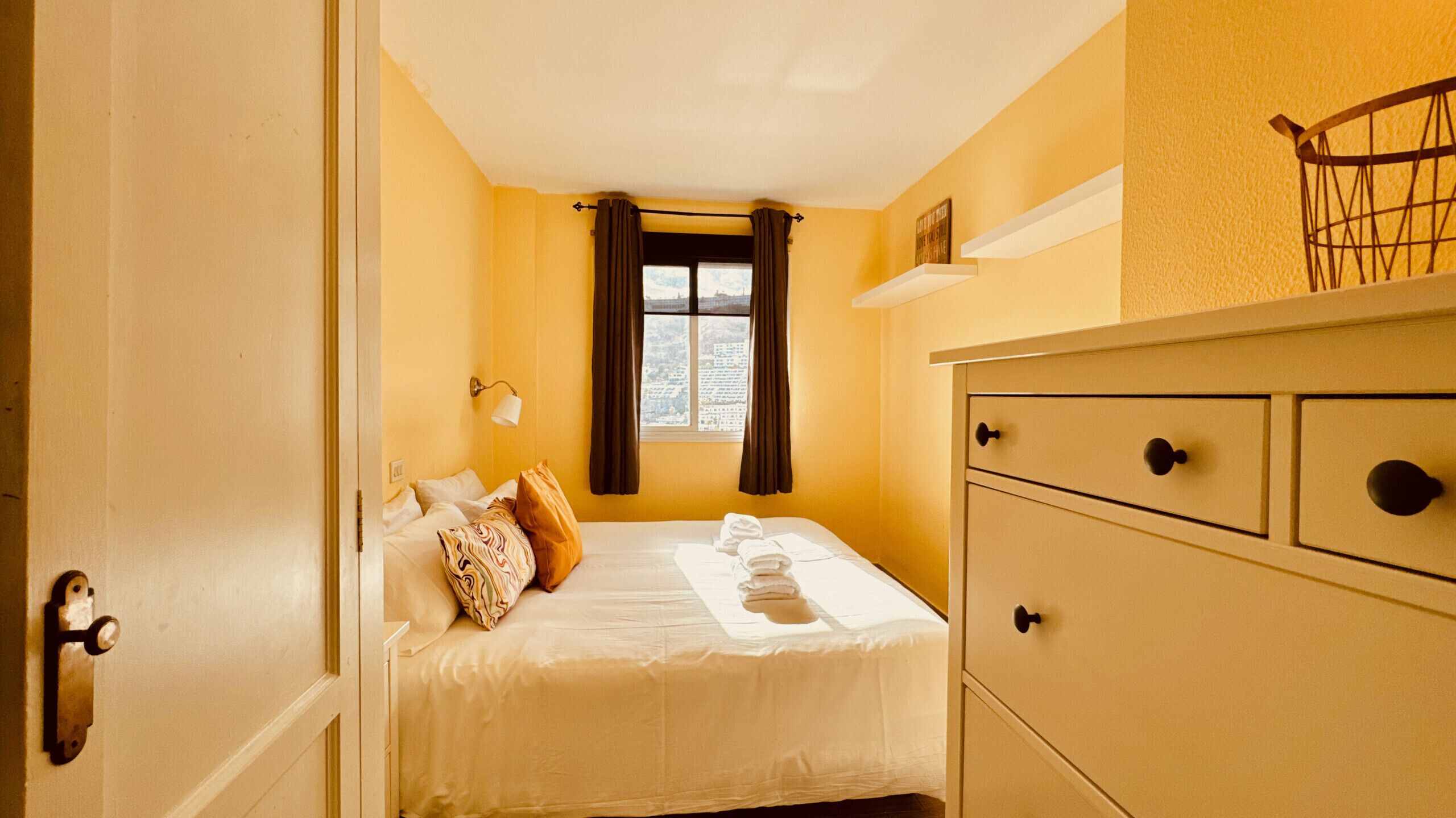 Une chambre d’hôtel avec un lit, une commode, une fenêtre avec des rideaux et une vue sur la ville.
