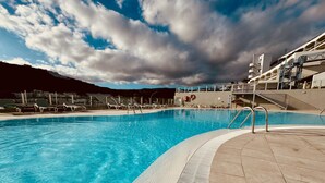 En swimmingpool med kristallklart blått vatten, omgiven av solstolar och en kakelbeklädd terrass.