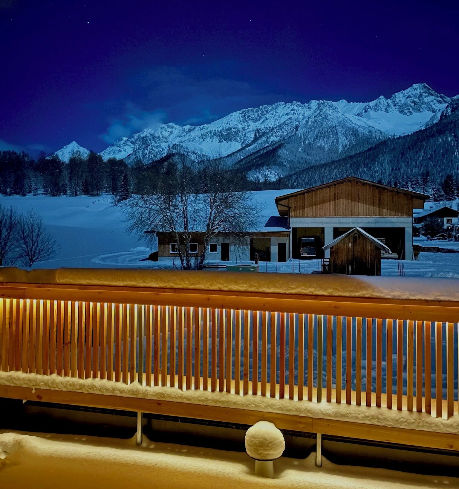 A snow-covered mountain landscape at night with a wooden building in the foreground.